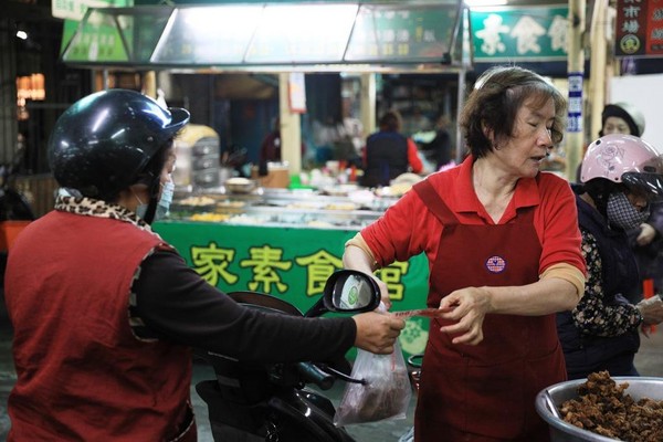 採買的婆媽們會把摩托車騎到攤子旁，一手百元鈔換一袋排骨酥，回家加菜。