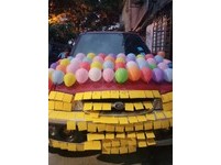 七彩的氣球被貼在一台紅色的汽車上，從引擎蓋、車身一路貼到車屁股，數一數氣球數量，引擎蓋上共40個，車身一側約可以黏47-50顆，兩邊共約100顆，加上車屁股約20個。