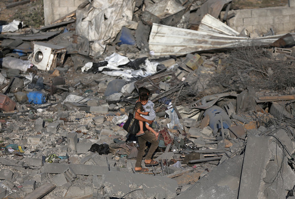 ▲▼以色列在加薩走廊發動空襲後，巴勒斯坦一名男孩抱著手足在殘骸中行走。（圖／路透）
