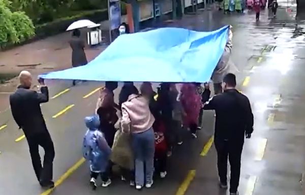 ▲教師用遮雨布幫幼兒園學生擋雨。（圖／翻攝閃電新聞）