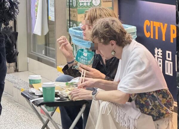 兩個老外蹲坐在超商外頭,把傘架當餐桌,吃起剛買來的食物。(翻攝「活網缺愛集散地4.0 」臉書社團)