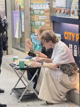 兩個老外蹲坐在超商外頭,把傘架當餐桌,吃起剛買來的食物。(翻攝「活網缺愛集散地4.0 」臉書社團)