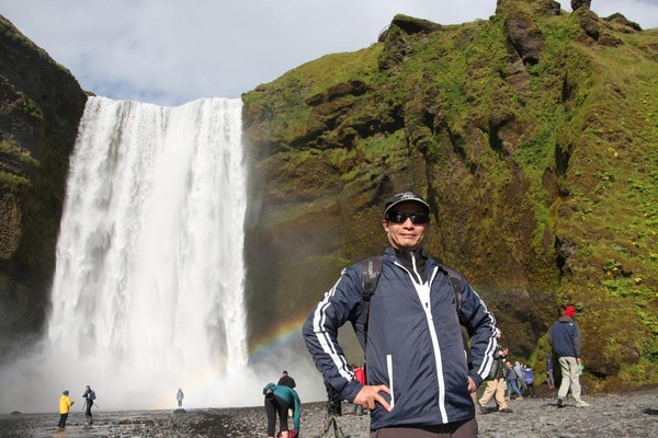 退休15年來，何文賢經常出國旅行，在冰島彩虹瀑布前留下美好記憶。（何文賢提供）