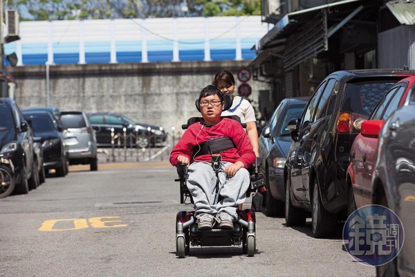 劉于濟（前）是極重度肌肉萎縮症患者，除了推動電動輪椅操控桿，其他都需外傭（後）協助。