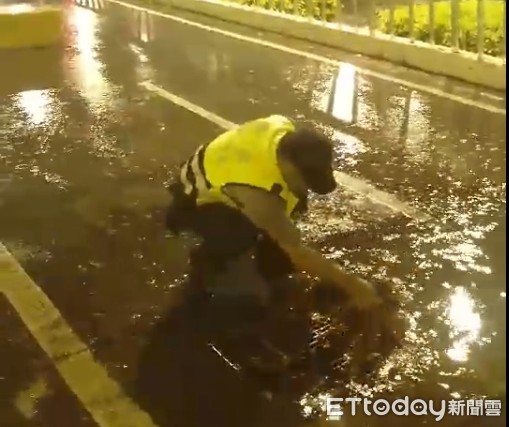 ▲一位員警在雨中，用手清理小東地下道機車道上排水孔的落葉，確保排水順暢。（圖／記者林悅翻攝）