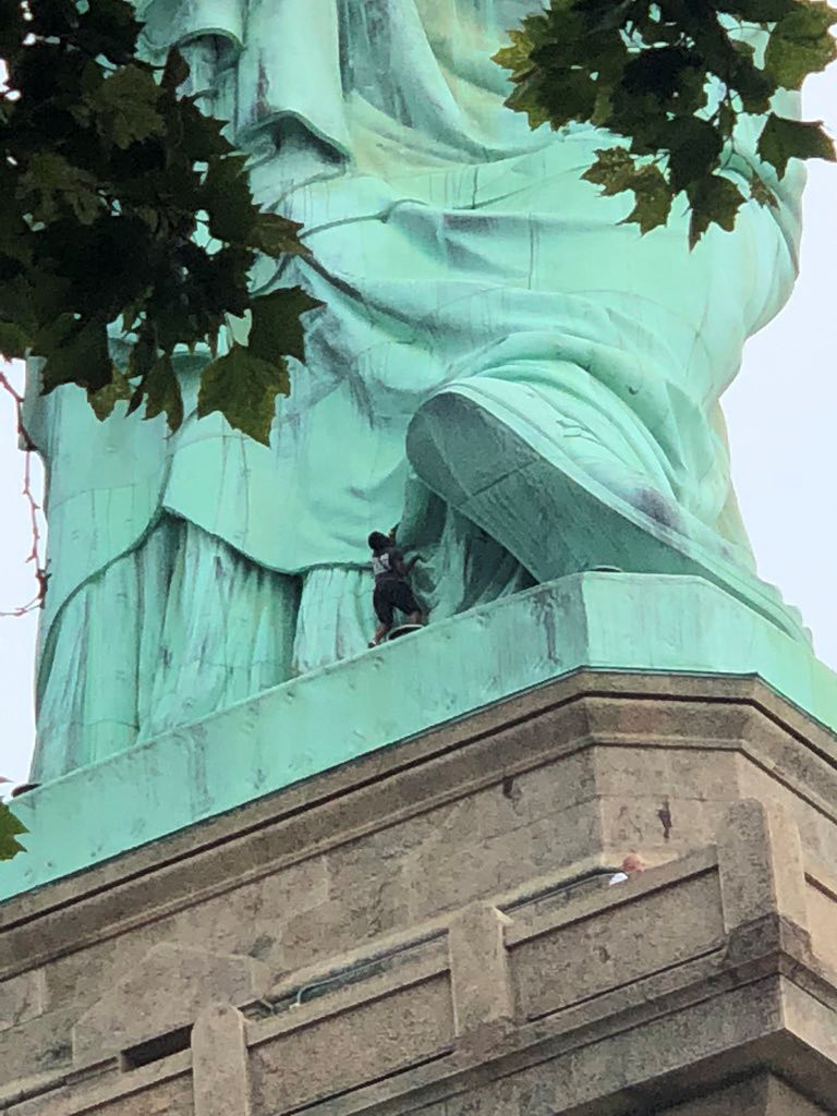 ▲▼紐約一名女子為抗議移民局政策，爬到自由女神像的裙底抗議（圖／路透社）