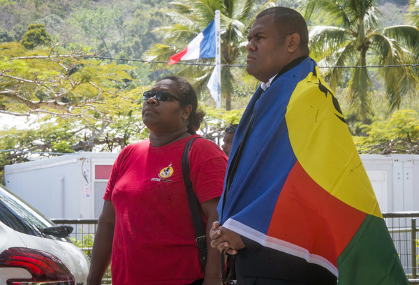 ▲▼一名身披新喀里多尼亞旗幟的男子和一名女子在投票所外排隊，法國國旗則在他們身後飄揚。（圖／達志影像／美聯社）