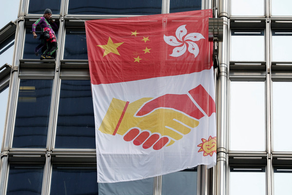 ▲法國蜘蛛人羅伯特掛出印有大陸國旗及香港區徽的巨型旗幟，下方還有緊握的雙手代表和平及溝通。（圖／路透社）