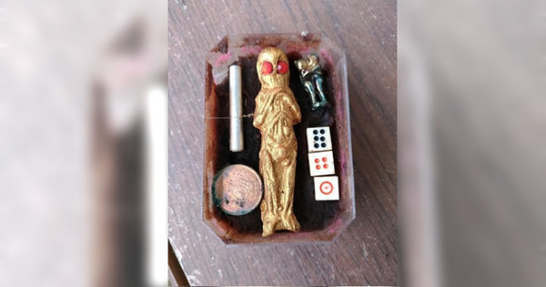 盒子裡放著一尊金色人像，且眼睛部分呈紅色，旁邊還放著錢幣、骰子、符管和正在親吻的男女人像。（圖／翻攝臉書）