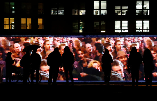 ▲▼遊客站在德國東邊畫廊的投影前，省思柏林圍牆倒塌前後的改變。（圖／路透）