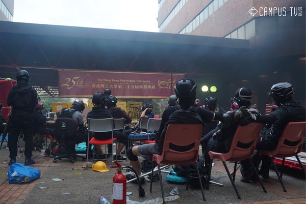 ▲示威者坐在理大畢業典禮橫幅前稍作休息。（翻攝自臉書「香港大學學生會校園電視」）