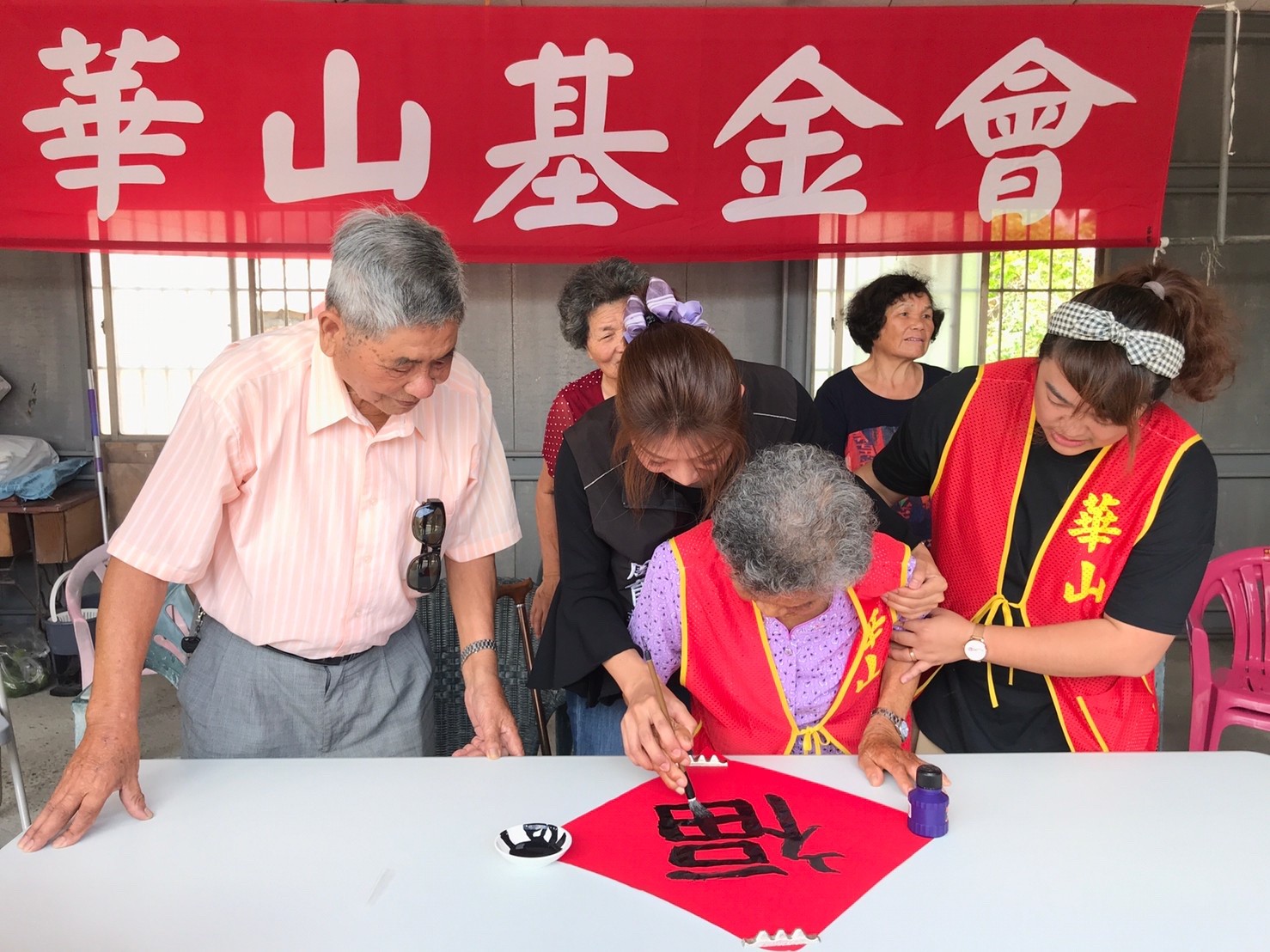 ▲褒忠鄉長秘書周育靖握著張林饁的手寫下一個「福」字。（圖／華山基金會褒忠愛心天使站提供）