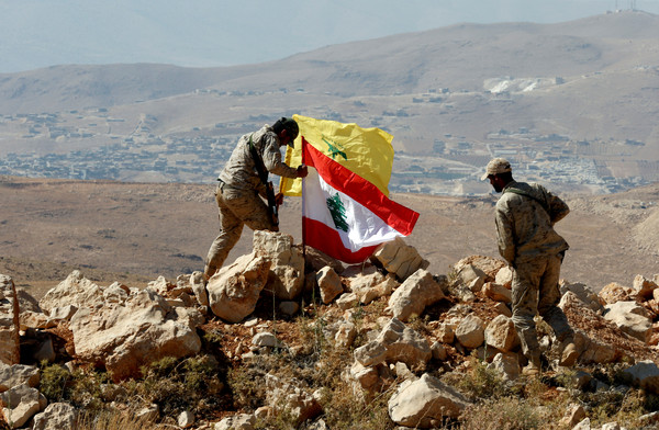 ▲真主黨士兵在黎巴嫩與敘利亞邊界掛上黎巴嫩國旗與真主黨旗幟。（圖／路透）