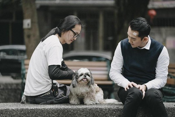 動物訓練師劉哥（左）安撫劇中的「里長狗」坐在公園矮牆上。右為施名帥。（酷斯本提供）