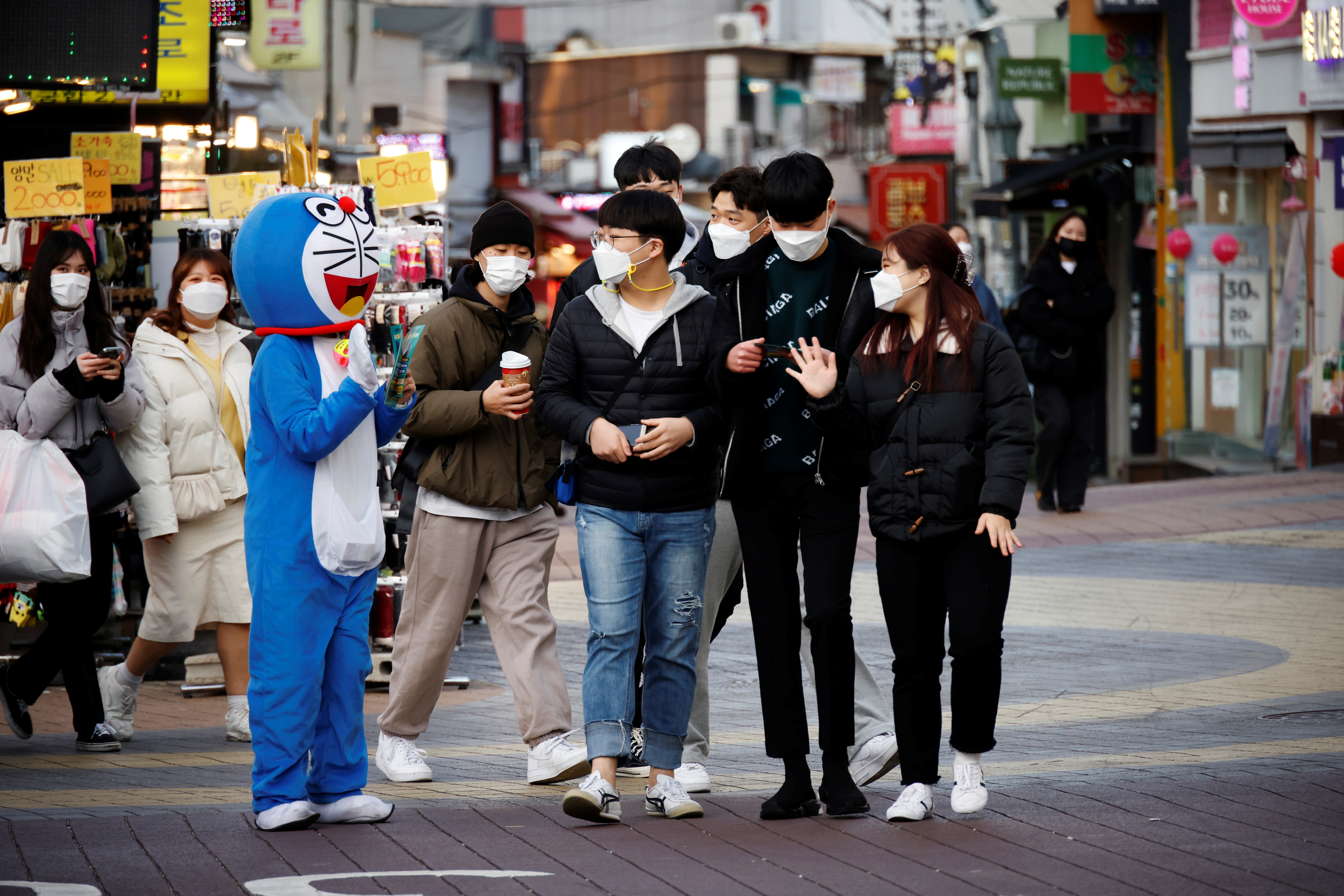 ▲▼首爾某商圈外，一名穿著哆啦A夢布偶裝的員工正向街頭的高中生攬客。（圖／路透社）