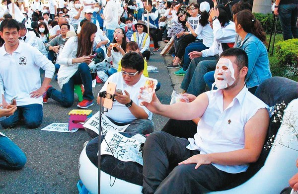 在反對同性婚姻的宗教團體集會上，四叉貓（前右）會自創各種怪招吸引媒體目光，瓜分輿論效應。圖為他躺在充氣床上直播敷面膜。（翻攝自四叉貓臉書／PNN）