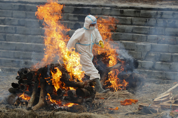 ▲新冠疫情急速惡化，尼泊爾也在燒屍體。圖為一名穿著防護衣的男子在兩堆焚燒屍體的柴火中穿過。(圖／達志影像／美聯社)