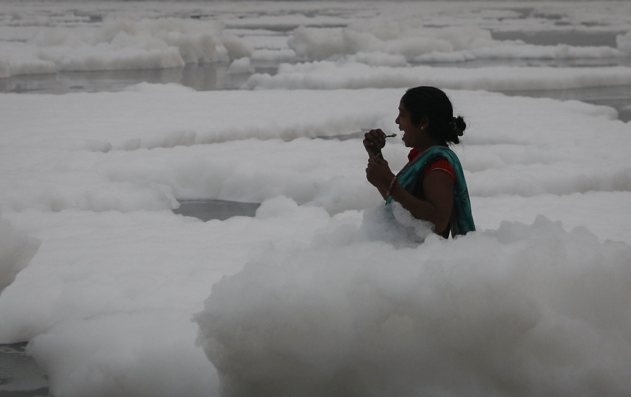 ▲▼印度首都新德里的「聖河」亞穆納河（Yamuna river）飄滿白色有毒泡沫，一名中年女性仍泡在河中，用河水刷牙。（圖／路透）