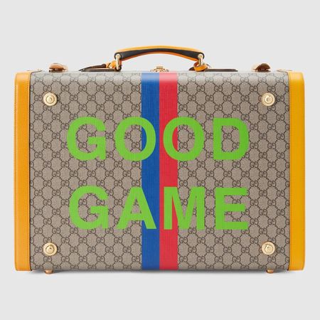 硬殼箱的表面材質為經典的米色Gucci Supreme帆布印花，飾有金色的扣環，以及用黃色皮革飾邊製成的箱緣，背後的GOOD GAME字樣，剛好呼應了Gucci經典的GG Logo。（Gucci 提供）