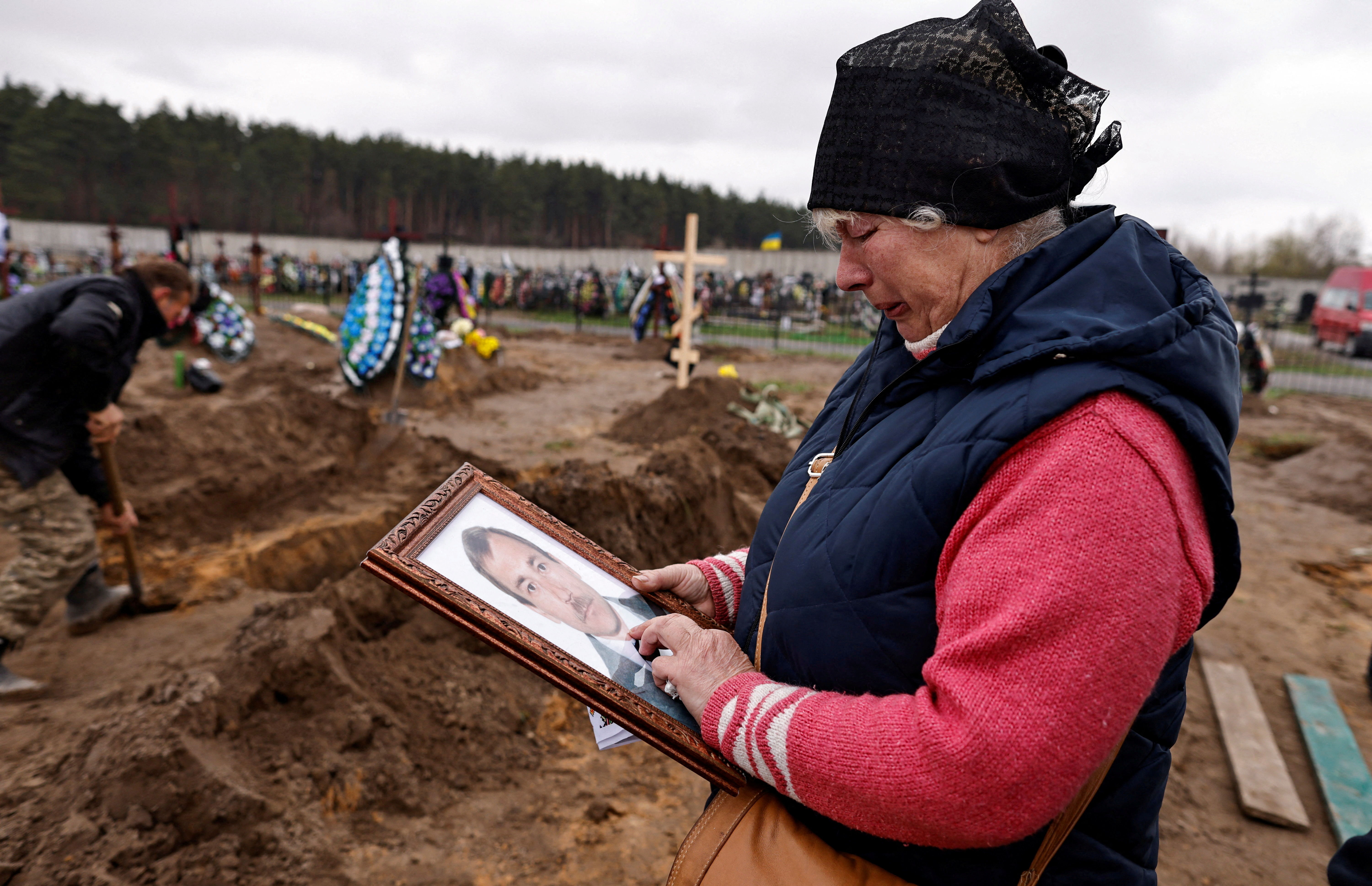 ▲▼烏克蘭布查57歲婦女在墳前，拿著丈夫的遺照哀悼，夫妻倆在俄軍砲轟建築物時遇難。（圖／路透社）