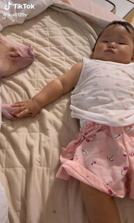嬰兒躺在床上準備入睡，伸手牽著粉紅豬的豬蹄共眠。（翻攝TikTok@yua0129y）