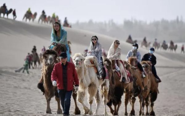 ▲月牙村村民帶著馴養的駱駝駝隊，載著遊客遊覽鳴沙山月牙泉景區。（圖／翻攝新華網）