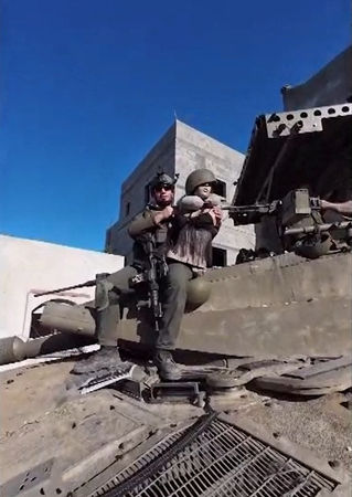 ▲▼路透社取得一段2024年2月26日發布的影片，截圖顯示一名以色列士兵坐在坦克上，手裡拿著一個穿黑色胸罩、戴軍盔的女性人體模型，據信拍攝地點是在加薩南部汗尤尼斯。（圖／路透）
