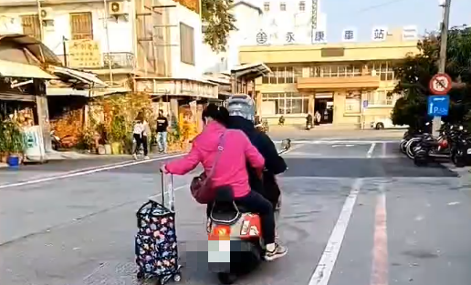 ▲台南市永康區中山路火車站前，有1部機車後載1名未戴安全帽女子，該女子手拉1個行李箱，在道路行駛滑行，影響行車安全。（圖／翻攝自社會事新聞影音，下同）