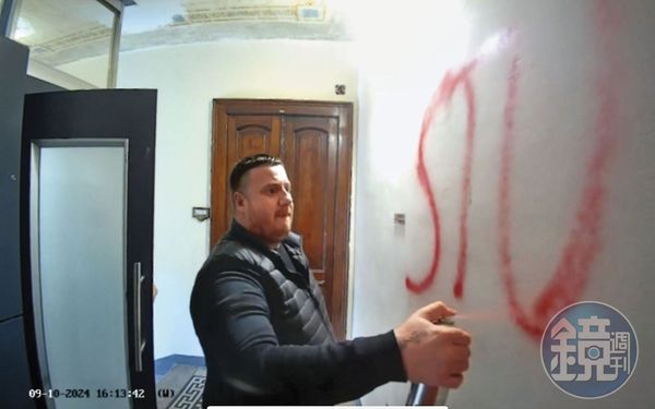 李穎家門口的監視器錄下噴漆者，此人噴完牆面，數秒後將監視鏡頭也噴成紅色。左側門後當時還藏有另一人。（李穎提供）