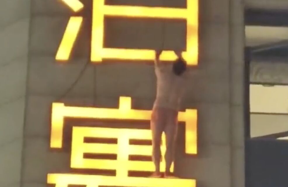 ▲大陸一名只穿內褲的男子掛在酒店外牆的招牌上，吸引路人目光。（圖／翻攝微博）