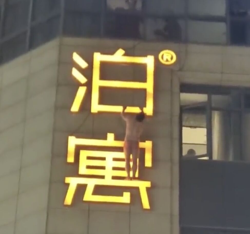 ▲大陸一名只穿內褲的男子掛在酒店外牆的招牌上，吸引路人目光。（圖／翻攝微博）