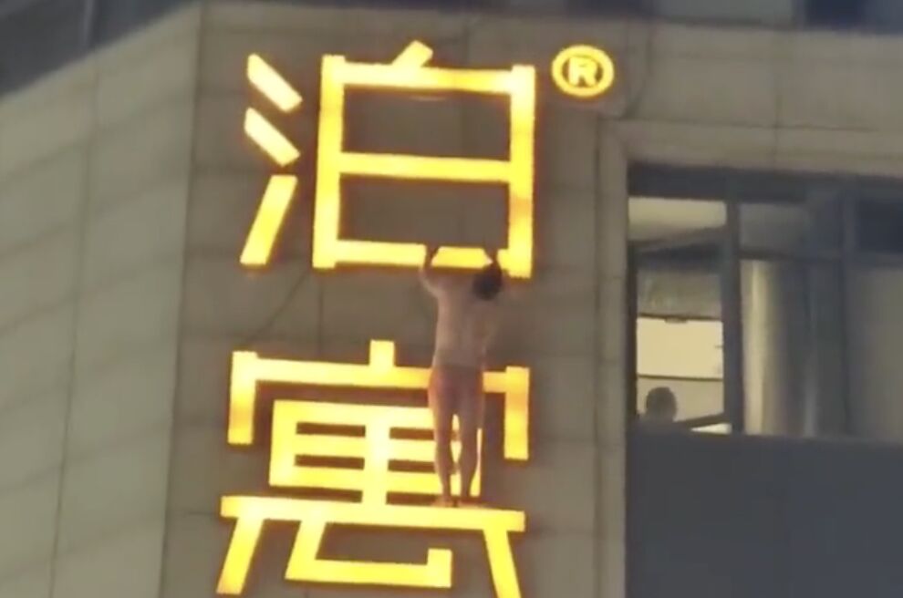 ▲大陸一名只穿內褲的男子掛在酒店外牆的招牌上，吸引路人目光。（圖／翻攝微博）