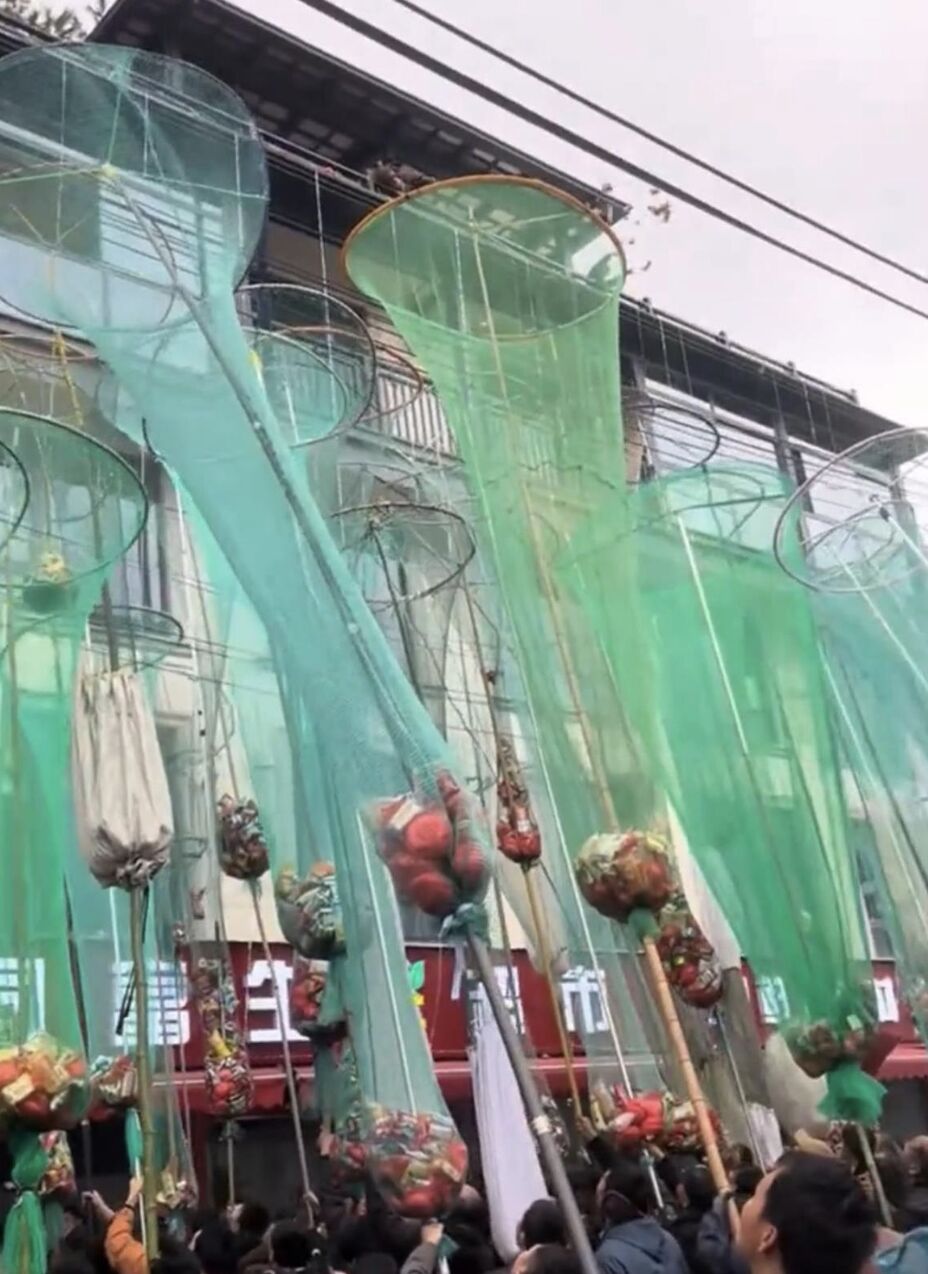 ▲浙江義烏一處新房上樑封頂大撒零食喜糖，民眾拿大型魚網「接喜」。（圖／翻攝極目新聞）