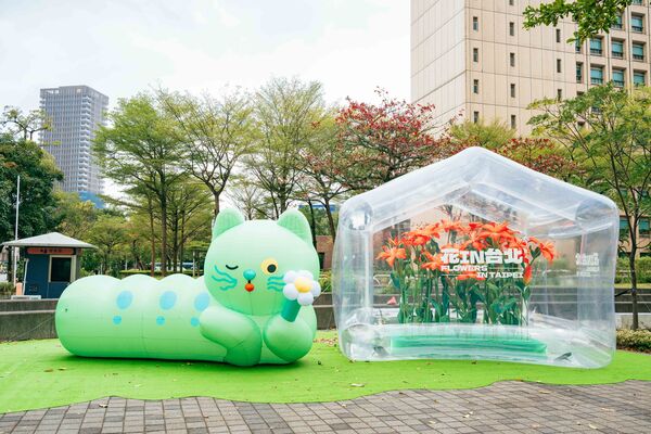 ▲「喵喵」氣偶於台北市政府東南角廣場首亮相，一旁設置透明的「春之幻境溫室」和百合紙藝，將展至3月1日。（圖／公園處提供）