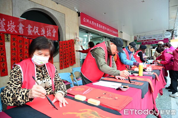 ▲書法名家在亞洲大學附屬醫院豐中分院現場揮毫，紅紙鋪展、墨香四溢，吸引民眾排隊領取春聯。（圖／記者游瓊華翻攝）
